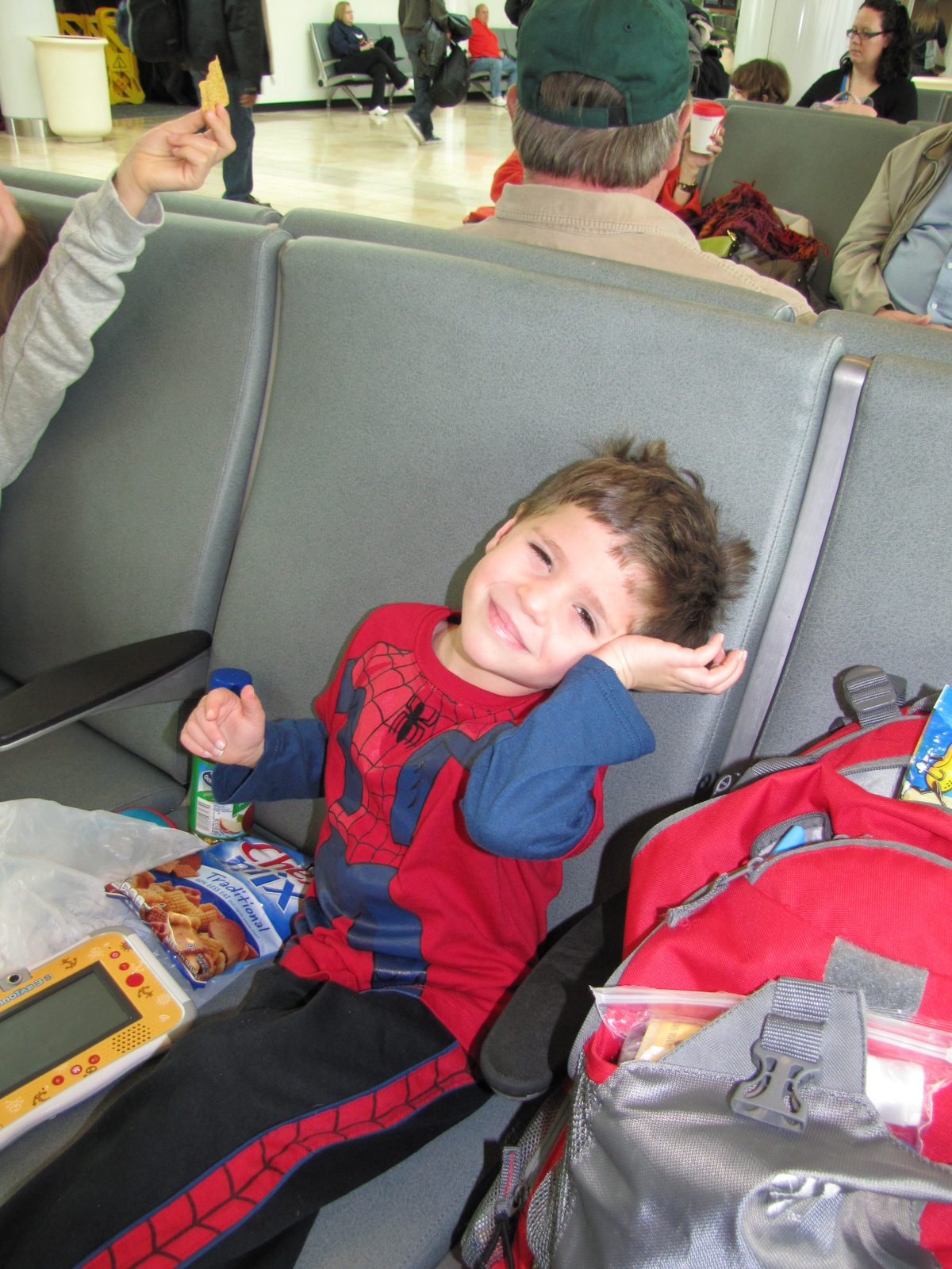 Thomas snacking at the gate, backpack beside him