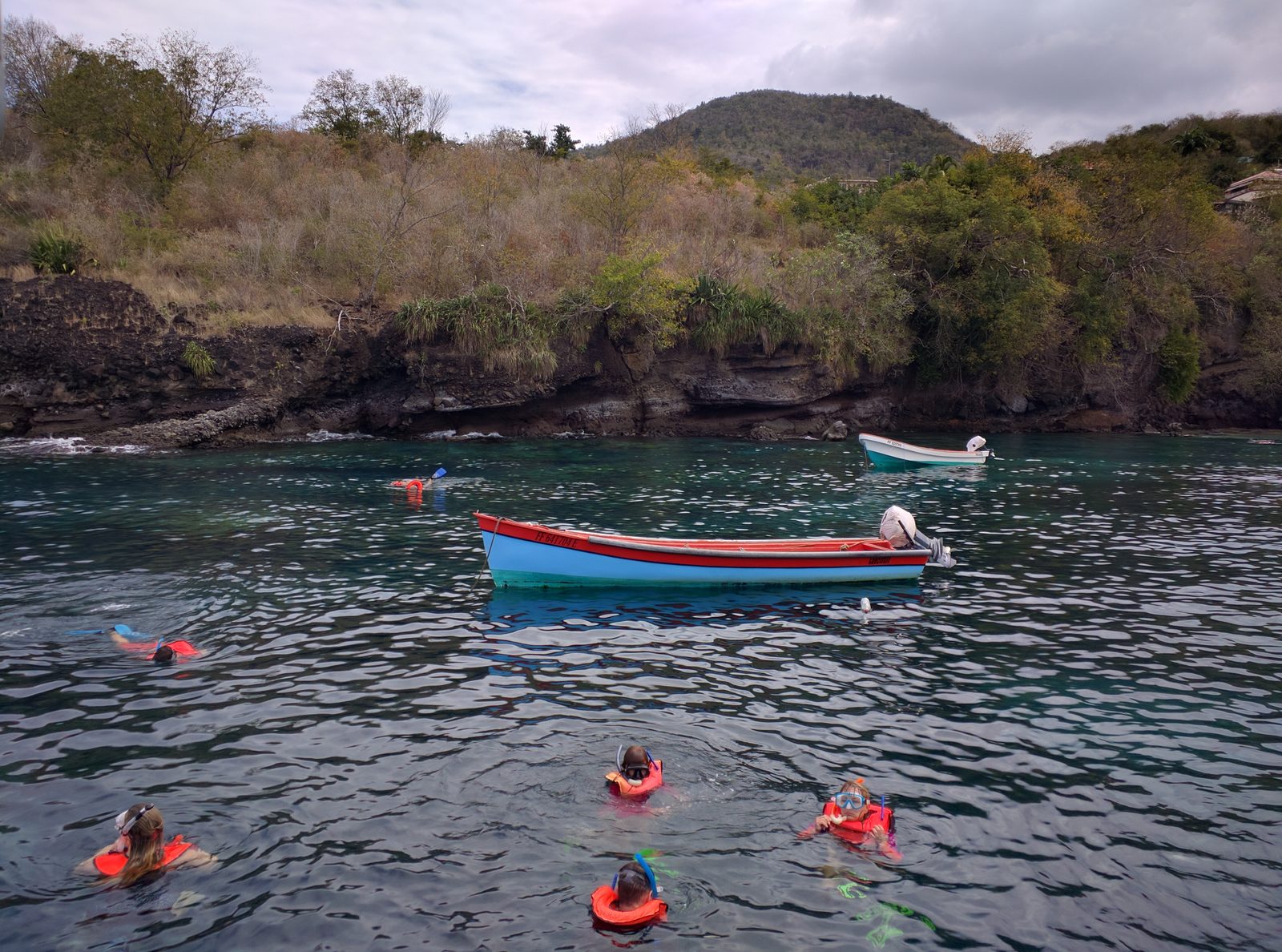 Snorkelers and a fishing boat in the cove at Anse Noire