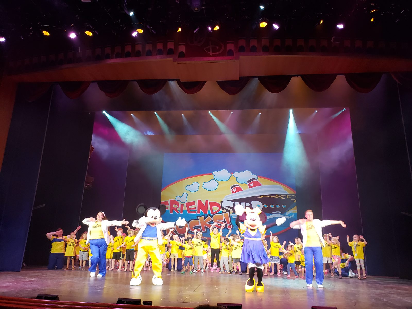 Mickey in his yellow outfit and Minnie in her blue dress on stage with the kids at Friend Ship Rocks