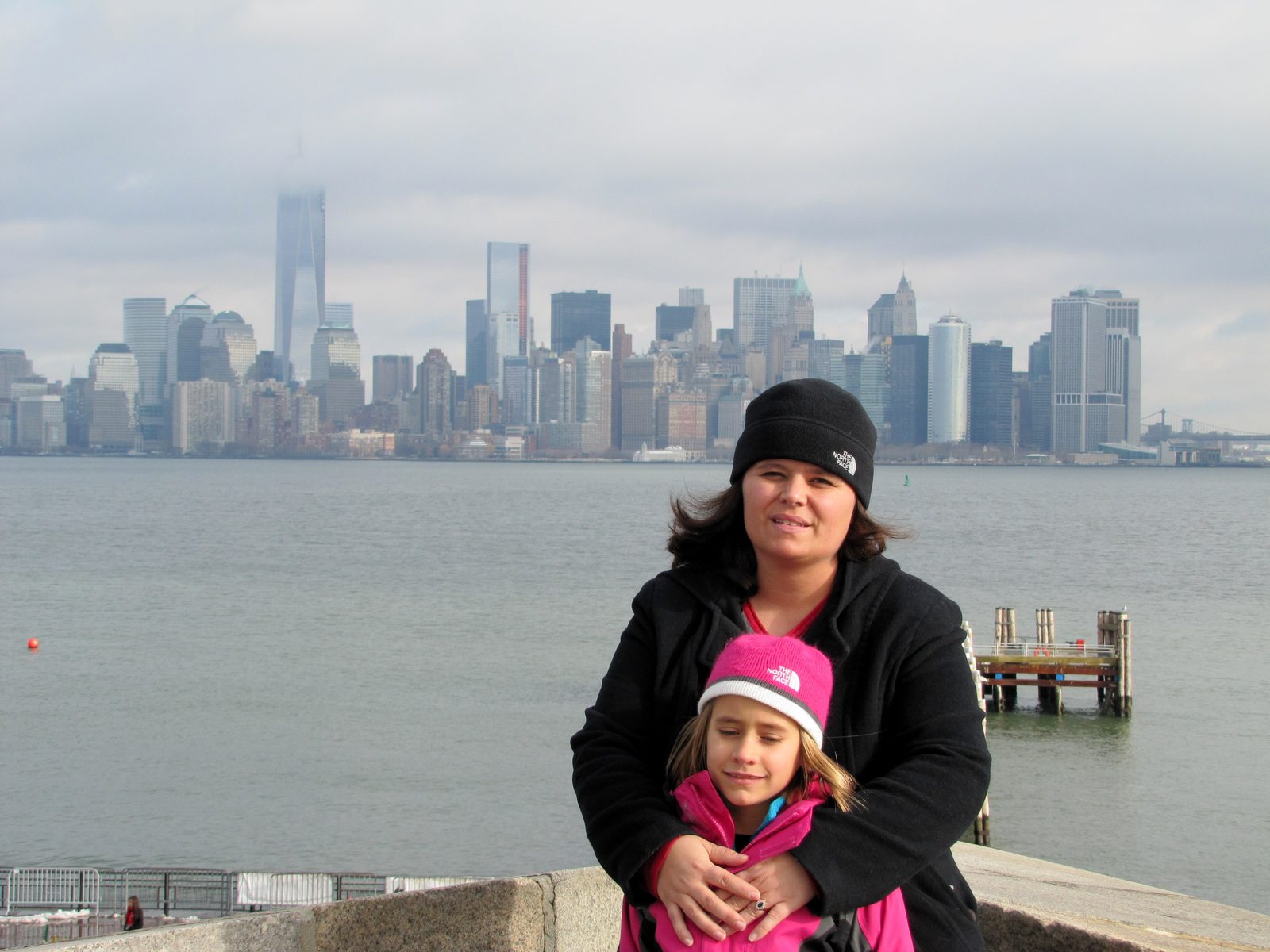 Kathy and Lisa bundled up by the harbor, city skyline behind them