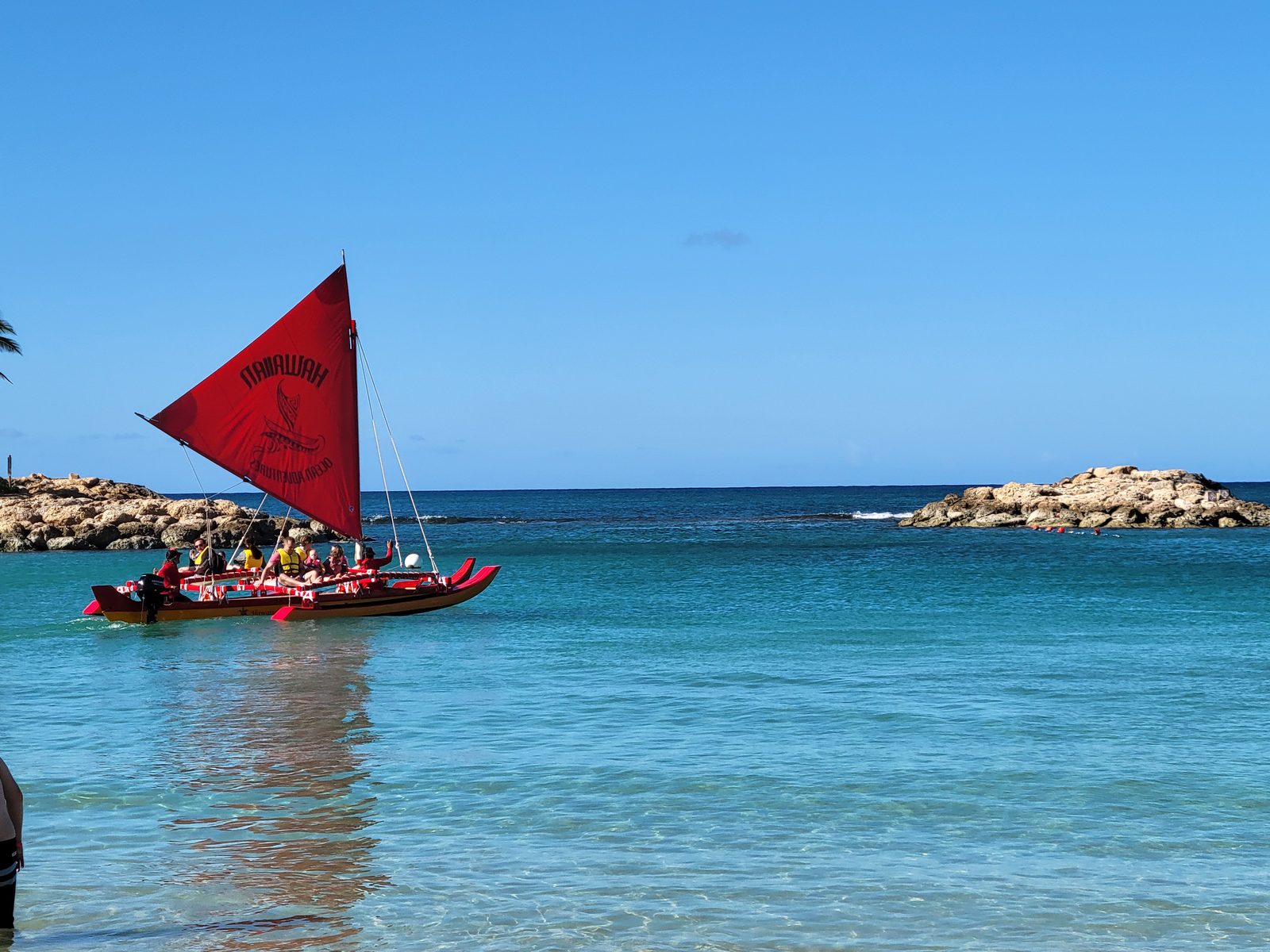 A red-sailed canoe crosses the lagoon