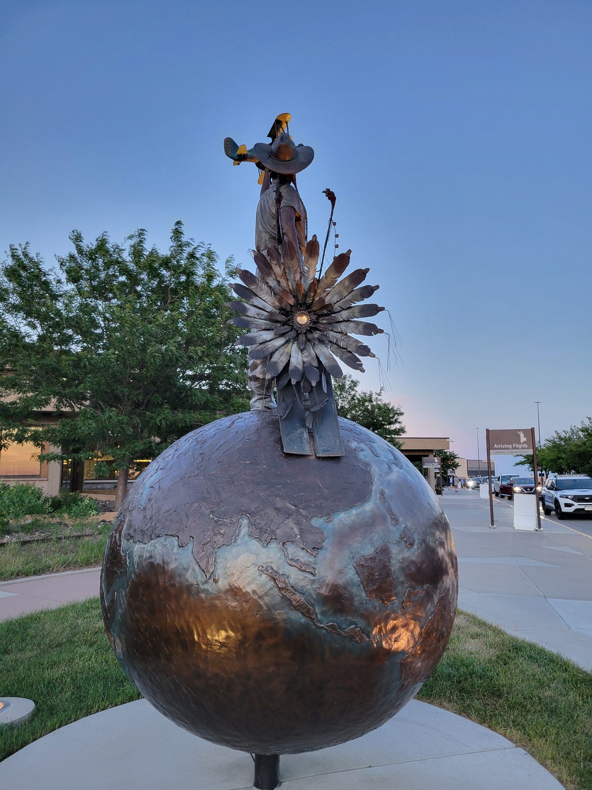 A sculpture of a figure on a bronze globe near the airfield