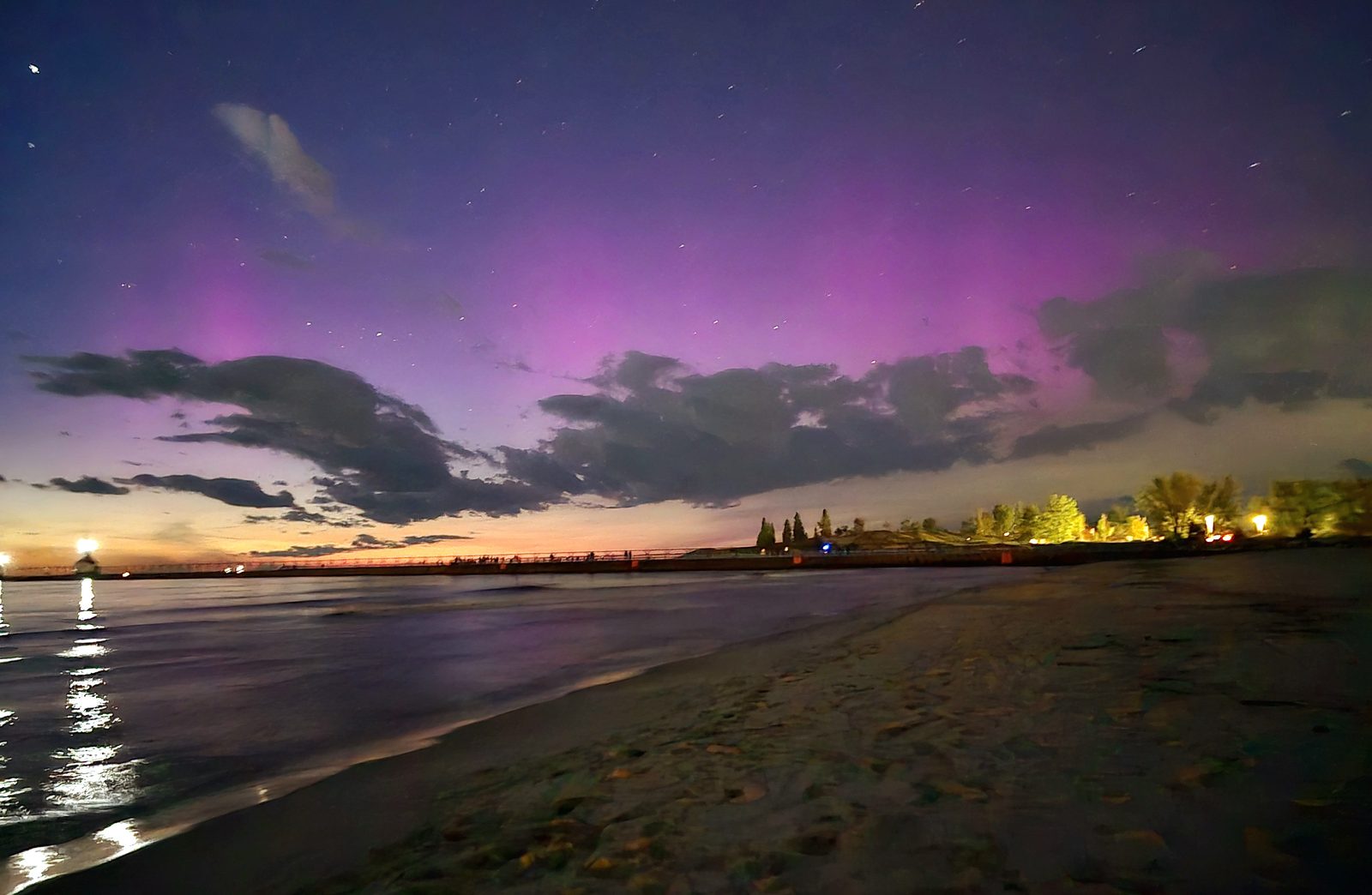 Pink aurora glowing above the clouds and the water